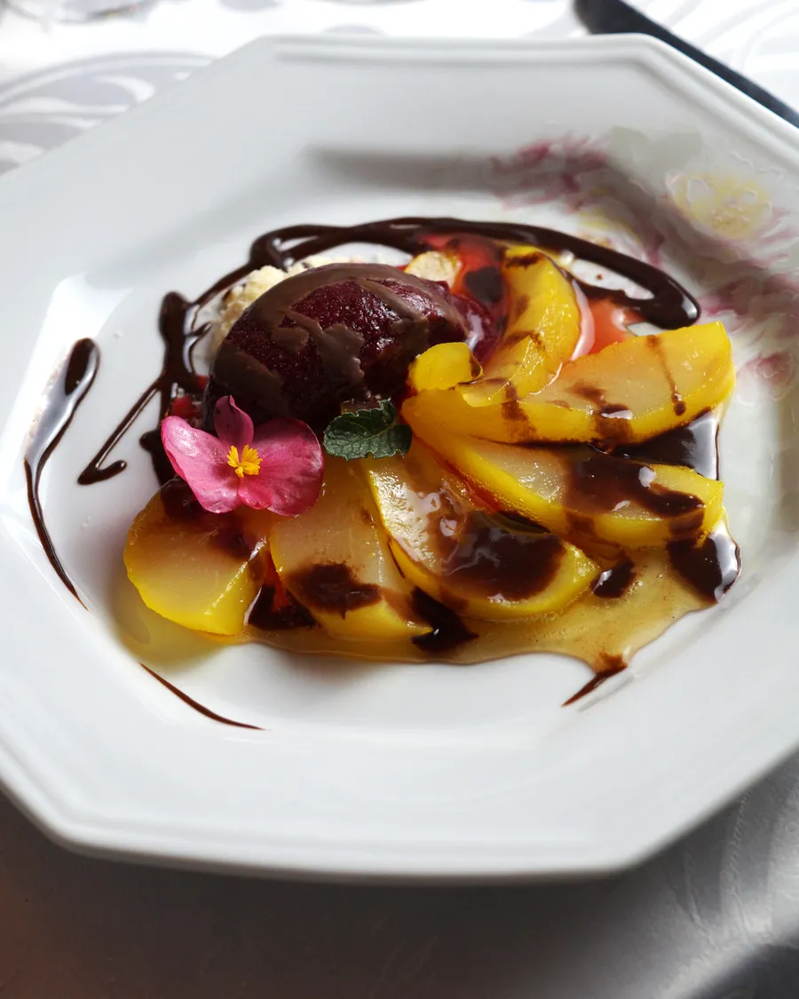 Lâminas de pera pochê com calda de chocolate, bola de sorbet de frutas vermelhas, folha de hortelã e flor comestível