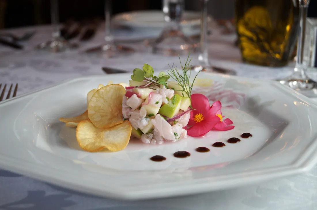 Tartare de peixe branco com maçã verde, chips de aipim, broto de endro e flor comestível cor-de-rosa em prato octogonal