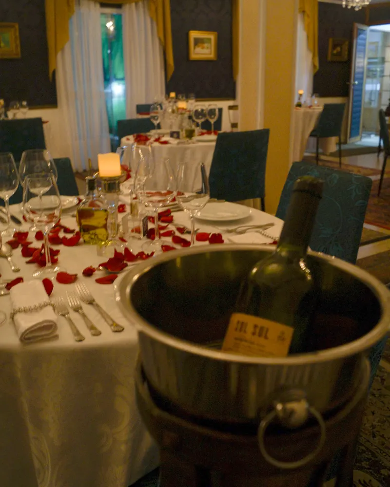 Mesas do salão decoradas com pétalas de rosa e balde de gelo com vinho