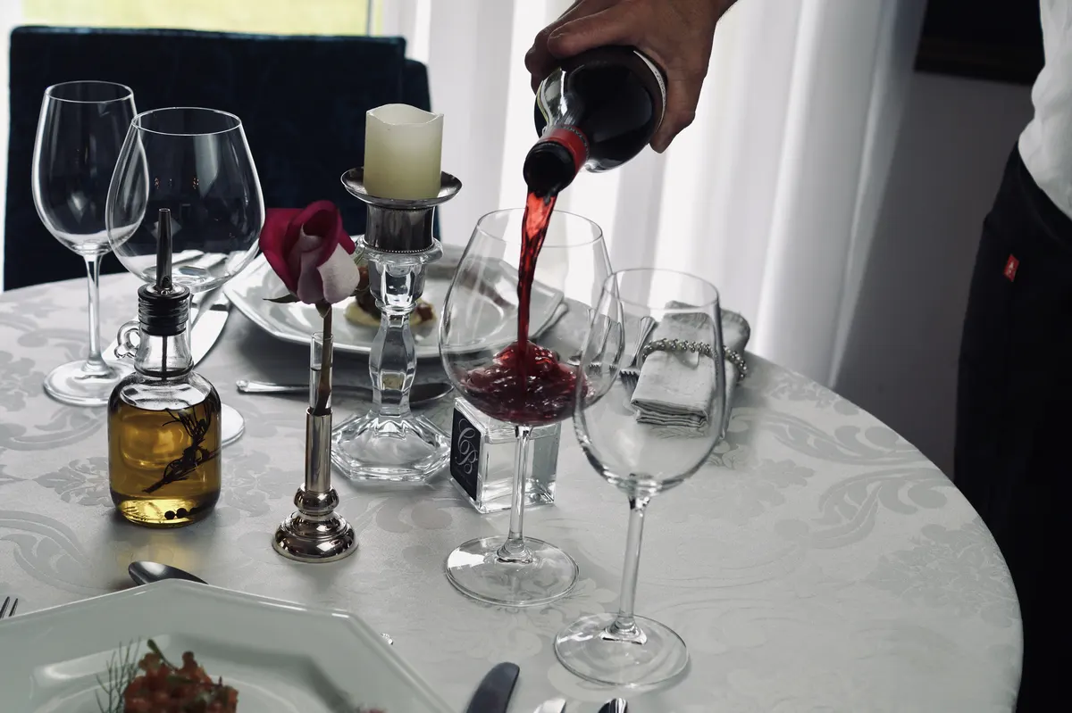 Vinho tinto sendo servido à mesa do Cordon Blanc, com rosa e vela acesa